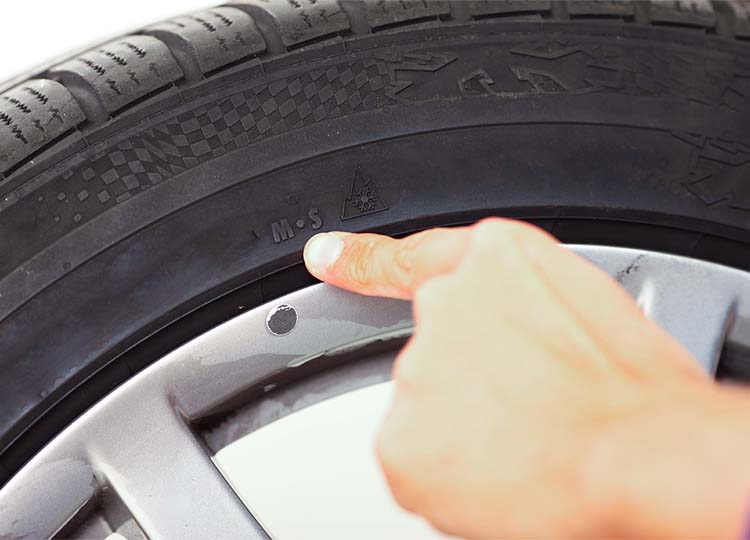 indication-des-logos-pneu-hiver Gros plan sur la main d'un mécanicien pointant du doigt les logo M+S et 3PMSF désignant un pneumatique adapté pour les conditions hivernales.